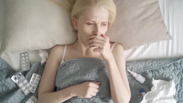 Sick young woman laying in bed. Woman with warm scarf on neck coughs and blows her nose. — Stock Video