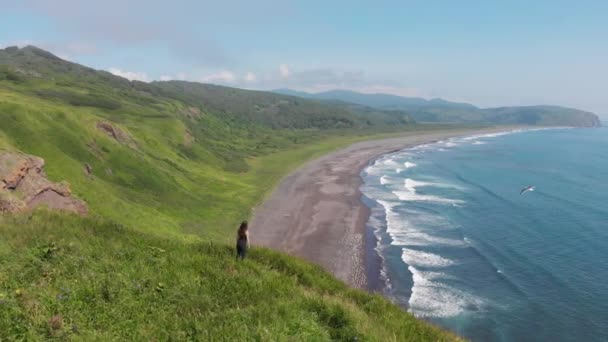Jovem mulher olhando para o oceano, de pé em um penhasco alto acima da praia de areia. — Vídeo de Stock