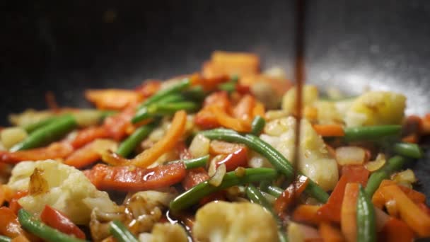 Ο σεφ στην κουζίνα χύνει σάλτσα σόγιας λαχανικών για γουόκ σε ένα τηγάνι, το οποίο τηγανίζεται και ανακατεύεται — Αρχείο Βίντεο