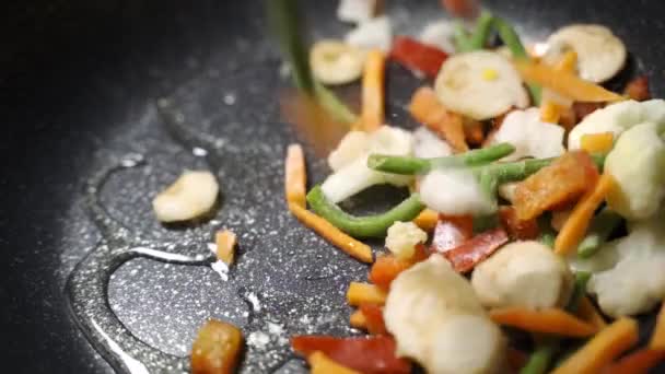Смешанные замороженные овощи в сковороде. Жаренье, тушение и перемешивание деревянной ложкой крупным планом. — стоковое видео
