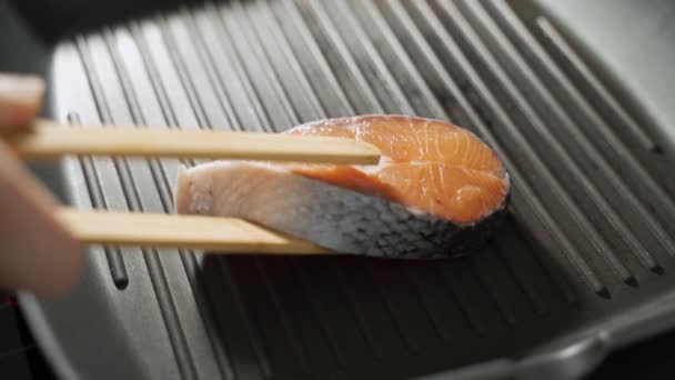 Рука чоловіка кладе шматочок лосося на гарячу сковороду. На чорному тлі — стокове відео
