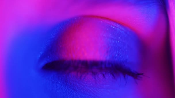 Extremt nära ögat iris under neonljus 4K. Kvinna med vacker makeup, glitter skuggor. Kvinnors ögon drar ihop sig. Nattliv, nattklubbskoncept — Stockvideo