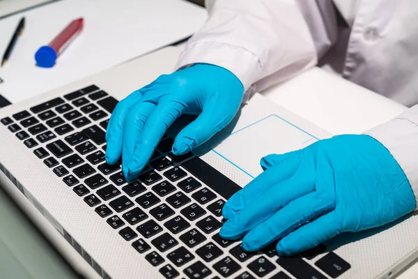 The doctors hands in medical gloves lie on the keyboard. The doctor is typing text on the computer. A medical worker writes out a sick leave electronically.