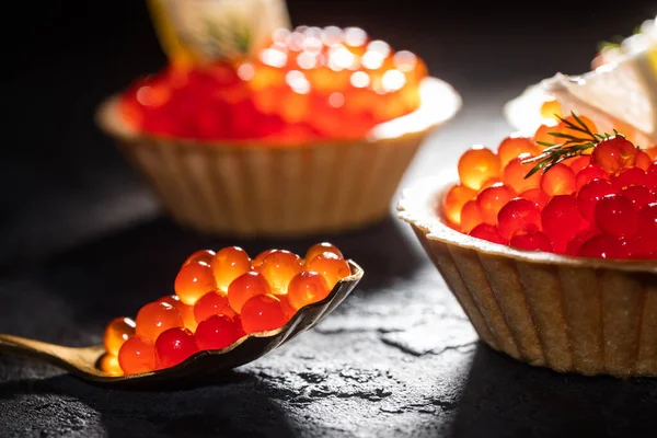 Caviar rojo en tartaletas sobre un fondo negro de cerca. Mariscos y sus propiedades beneficiosas. Fotos de stock