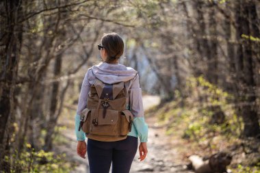 Güneş gözlüklü, büyük sırt çantalı bir kadın orman yolunda durup etrafına bakıyor. Tek başına yürü..