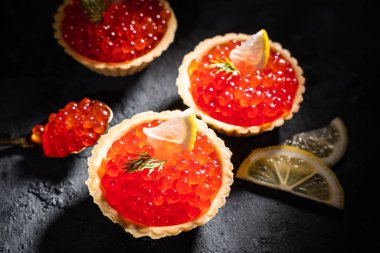 Turtaların içinde kırmızı havyar. Siyah arka planda limon dilimleri olan kırmızı havyar..