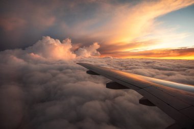 Uçak penceresinden nefes kesici bir manzara. Bulutların üstünde uçak kanadı. Gün batımının kuş bakışı görüntüsü. Seyahat ve turizm