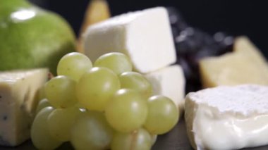 Dilimlenmiş peynir, fındık, üzüm, bal ve bıçak tabakta. Sayfa arkaplanında döndürme