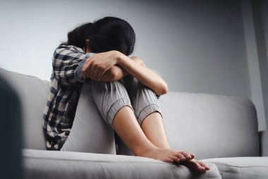 Mutsuz, bunalımlı kadın koltukta oturuyor ve elleriyle yüzünü kapatıyor. Depresyon kavramı.