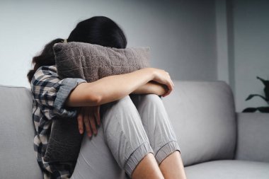 Mutsuz, üzgün, üzgün kadın kanepede oturuyor ve yüzünü yastığa gizliyor. Depresyon konsepti.