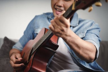 Yakışıklı Asyalı adamın oturma odasında gitar çalışmasının ya da gitar çalmasının keyfini çıkarın. 