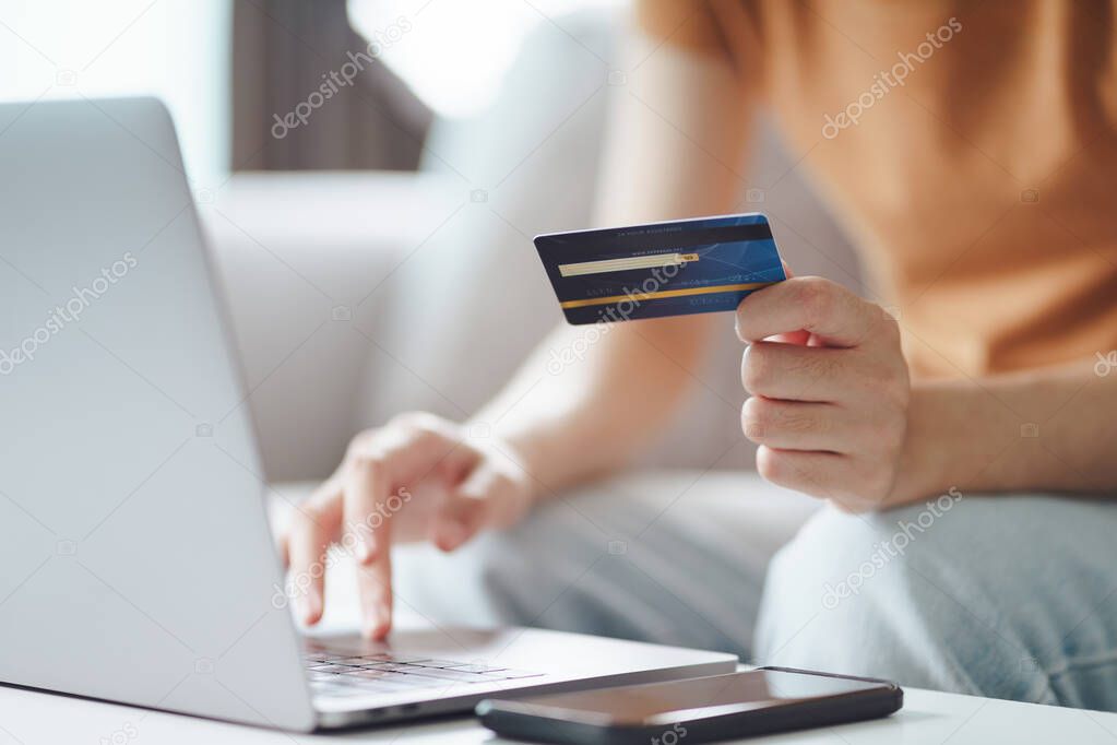 Young woman holding credit card and using laptop computer. Online shopping, internet banking, e-commerce, spending money, working from home concept