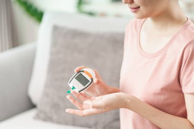 Asyalı kadın kan şekeri seviyesini dijital glikoz ölçer, sağlık ve sağlık sigortası, diyabet, glisemi konseptine göre kontrol ediyor.