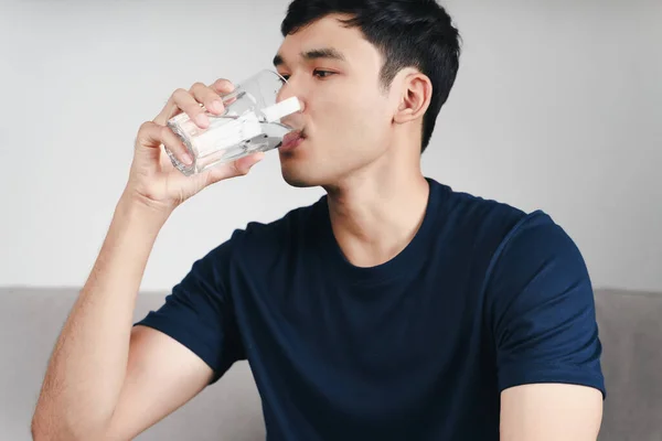 handsome asian man drinking a glass of water on the sofa at living room