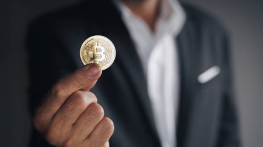Siyah takım elbiseli yakışıklı yatırımcı elinde kara arka plan, ticaret, kripto para, dijital sanal para, alternatif finans ve yatırım kavramı üzerine altın bir bitcoin tutuyor.