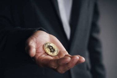 Siyah takım elbiseli yakışıklı yatırımcı elinde kara arka plan, ticaret, kripto para, dijital sanal para, alternatif finans ve yatırım kavramı üzerine altın bir bitcoin tutuyor.