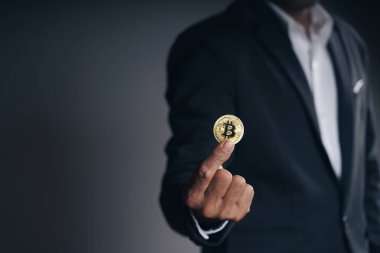 Siyah takım elbiseli yakışıklı yatırımcı elinde kara arka plan, ticaret, kripto para, dijital sanal para, alternatif finans ve yatırım kavramı üzerine altın bir bitcoin tutuyor.