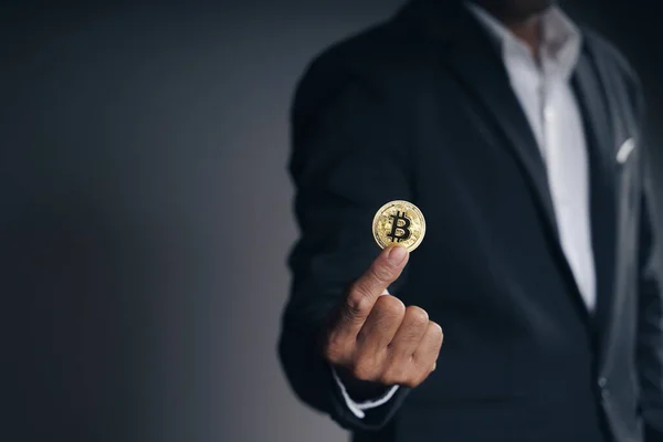 Handsome Investor Businessman in black suit holding a golden bitcoin on dark background, trading, Cryptocurrency, Digital virtual currency, alternative finance and investment Concept
