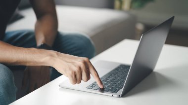 Evdeki kanepede oturan genç adam internet, serbest çalışan, rahat, modern iş hayatı tarzını kullanan ve evde çalışmak için dizüstü bilgisayarın klavyesindeki enter tuşuna basar.