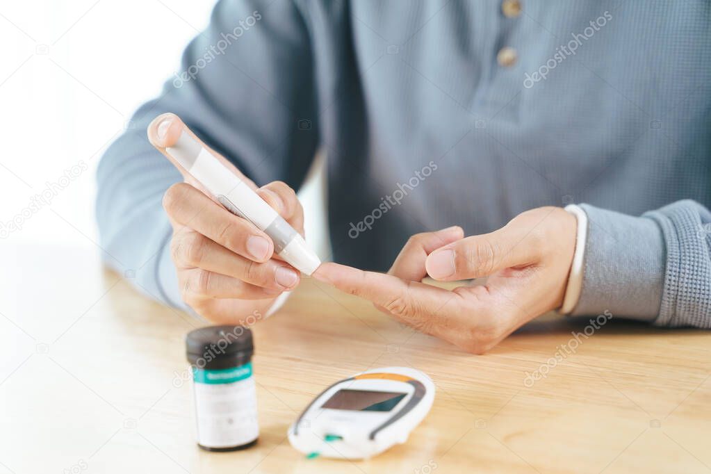 Asian man using lancet on finger for checking blood sugar level by Glucose meter, Healthcare and Medical, diabetes, glycemia concept