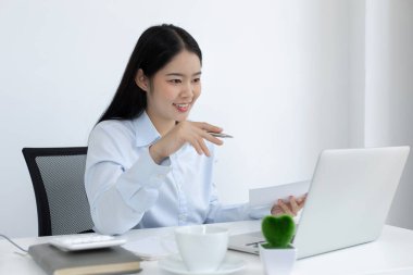 Asyalı kadın internet üzerinden neşeli bir gülümsemeyle çalışıyor, evde kalıyor, Yeni Normal, Covid-19 Coronavirus, Sosyal Mesafe, İnternet Öğrenimi.