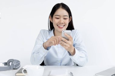 Asyalı kadın çalışanlar akıllı telefonlar aracılığıyla pazar verilerini analiz ediyorlar ve şirketin finansmanını hesaplamak için dizüstü bilgisayarları evde, evde ve yeni normal kavramlarla çalışan özel bir ofiste bulunuyorlar..