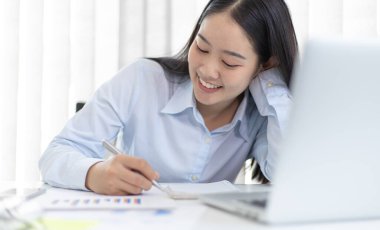 Asyalı kadın internet üzerinden neşeli bir gülümsemeyle çalışıyor, evde kalıyor, Yeni Normal, Covid-19 Coronavirus, Sosyal Mesafe, İnternet Öğrenimi.