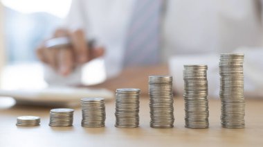 Bir grafiğe yerleştirilmiş dolar sikkeleri, hesap makinesine basan bir iş adamının bulanık görüntüsü, mali iş büyümesi, tasarruf para kavramı