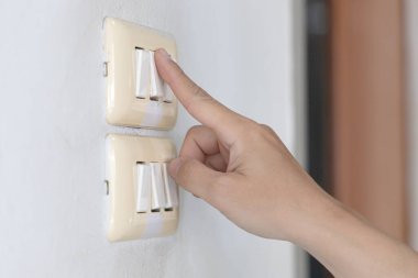 Genç adamın elini kapat, düğmeye bas ve ışık düğmesini aç. Duvarın yanındaki elektrik devresini aç..