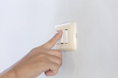 Genç adamın elini kapat, düğmeye bas ve ışık düğmesini aç. Duvarın yanındaki elektrik devresini aç..