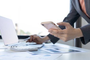Finans çalışanları şirketin finansal verilerini bir dizüstü bilgisayarda inceliyor ve akıllı telefonları kullanarak sosyal uzaklıktaki ekiple iletişim kuruyor veya sohbet ediyor, virüs salgını sırasında çalışıyor.