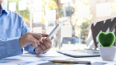 Finans çalışanları şirketin finansal verilerini bir dizüstü bilgisayarda inceliyor ve akıllı telefonları kullanarak sosyal uzaklıktaki ekiple iletişim kuruyor veya sohbet ediyor, virüs salgını sırasında çalışıyor.