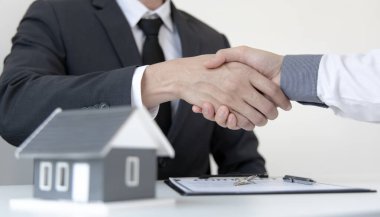 Emlakçılar ve müşteriler, arazi, sigorta, tokalaşma ve iyi tepki konsepti olan bir ev satın alma sözleşmesini imzaladıkları için tebrik etmek için el sıkışıyorlar..