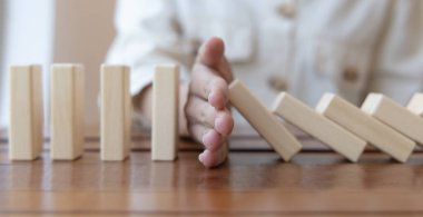 İş kadını sürekli risk almak, sürekli hasar azaltmak, iş dominosu başarısızlıklarını durdurmak için domino taşının üzerine düşen elleri durdurur..