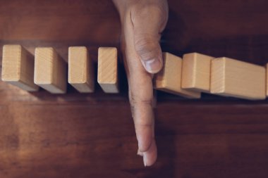 İş kadını sürekli risk almak, sürekli hasar azaltmak, iş dominosu başarısızlıklarını durdurmak için domino taşının üzerine düşen elleri durdurur..