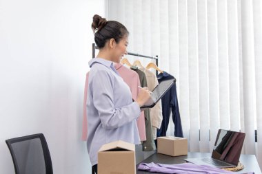 Genç Asyalı bir kadın, kıyafetlerini internetten tabletle almak isteyen bir müşteriye gülümseyerek sohbet ediyor ve anlaşmayı, sosyal medya alışverişini veya internet alışverişini onaylıyor..