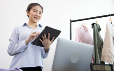 Genç Asyalı bir kadın, kıyafetlerini internetten tabletle almak isteyen bir müşteriye gülümseyerek sohbet ediyor ve anlaşmayı, sosyal medya alışverişini veya internet alışverişini onaylıyor..