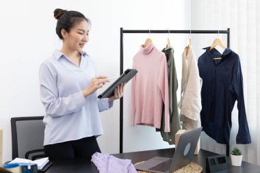 Genç Asyalı bir kadın, kıyafetlerini internetten tabletle almak isteyen bir müşteriye gülümseyerek sohbet ediyor ve anlaşmayı, sosyal medya alışverişini veya internet alışverişini onaylıyor..