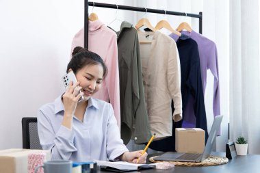 Asyalı iş kadını internetten sipariş alıyor ve siparişlerini, çevrimiçi giyim satış işlerini, sosyal medyada kıyafet satma veya internet üzerinden satış işlerini onaylamak için müşterilerle sohbet ediyor..