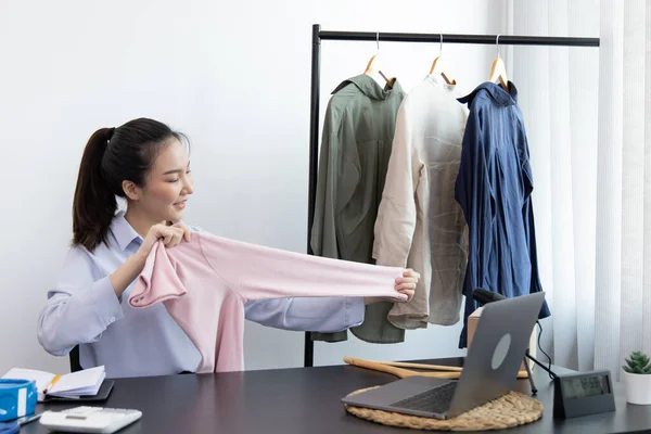 Young Asian women show off the clothes customers want to see through a live performance with a laptop, Selling things through video recording or live shows via the Internet, Top business.