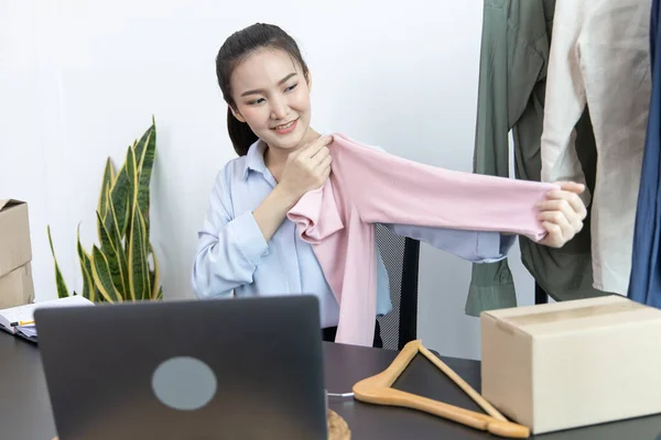 Young Asian women show off the clothes customers want to see through a live performance with a laptop, Selling things through video recording or live shows via the Internet, Top business.