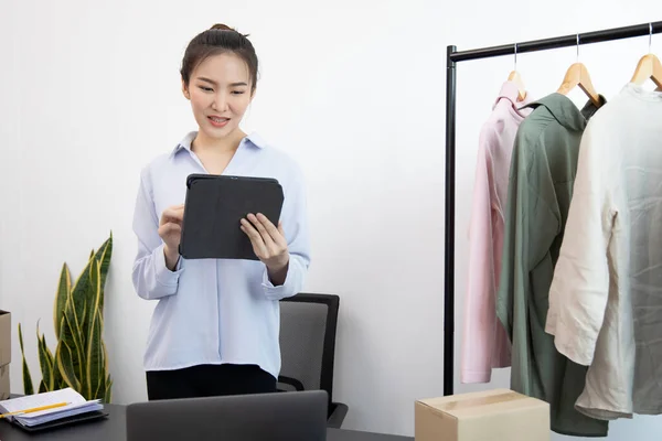 Young Asian woman chatting with a bright smile to a customer who wants to buy her clothes online with a Tablet and confirms the order to close the deal, Social media trading or online shopping.