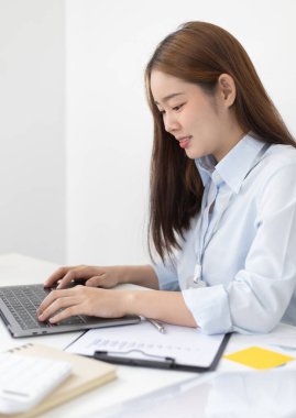 Genç Asyalı ofis çalışanı finansal verileri analiz etmek ve çalışmalarını özetlemek için dizüstü bilgisayara elini basıyor. Ofis çalışanları, mavi gömlekli güzel bayan çalışanlar..