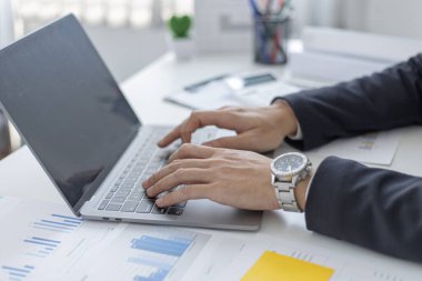 Genç Asyalı ofis çalışanı finansal verileri analiz etmek ve çalışmalarını özetlemek için dizüstü bilgisayara basıyor. Ofis çalışanları, siyah takım elbiseli yakışıklı erkek çalışanlar..