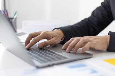 Genç Asyalı ofis çalışanı finansal verileri analiz etmek ve çalışmalarını özetlemek için dizüstü bilgisayara basıyor. Ofis çalışanları, siyah takım elbiseli yakışıklı erkek çalışanlar..