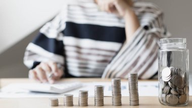 Eğik bir grafiğe yerleştirilmiş dolar sikkeleri, hesap makinesine basan bir iş kadınının bulanık görüntüsü, mali iş büyümesi, iş büyümesi veya uzun vadeli kazanç için tasarruf etmek, para tasarrufu..