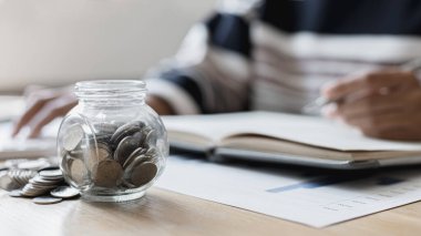 Eğik bir grafiğe yerleştirilmiş dolar sikkeleri, hesap makinesine basan bir iş kadınının bulanık görüntüsü, mali iş büyümesi, iş büyümesi veya uzun vadeli kazanç için tasarruf etmek, para tasarrufu..