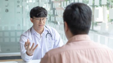 Beyaz cüppeli genç Asyalı bir adam bir adamla konuşuyor, doktorlar hastalıklara teşhis koyuyor ve hastane muayene odasındaki hastalara tavsiye ya da tedavi çözümleri sunuyor..