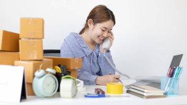 İnternette ürün satan genç bir kadın telefonda arayıp listeyi bir not defterine yazan bir müşteriden sipariş almak için konuşuyordu..