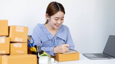 Genç Asyalı kadın, bilgilere göre nakliyeye hazırlanmak için müşterinin bilgilerini ve adreslerini not defterine yazıyor..